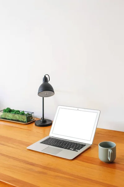 Laptop and cup on wooden standing desk near light wall