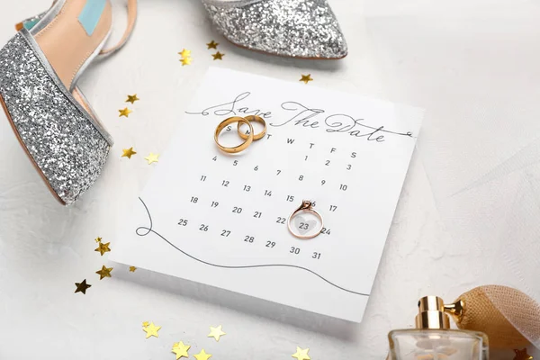 Calendar with marked date, wedding rings and stylish female accessories on light table