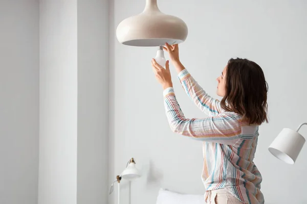 Kobieta Wymieniająca Żarówkę Lampie Wiszącej Domu — Zdjęcie stockowe
