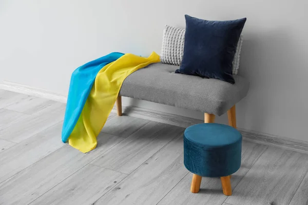 Bench with Ukrainian flag, cushions and pouf near light wall