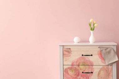 Pembe duvarın yanındaki vazoda taze lalelerle süslü şık çekmeceler.