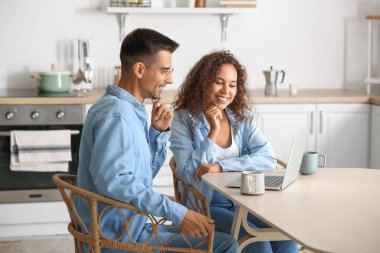 Mutfakta modern dizüstü bilgisayar kullanan mutlu genç çift.