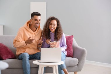 Young couple with popcorn watching movie on laptop at home