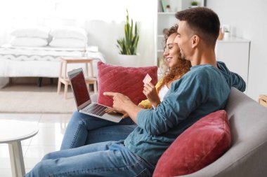 Genç çift evdeki kanepede internetten bir şeyler sipariş ediyor.