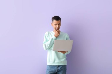 Leylak arkaplanda dizüstü bilgisayar kullanan düşünceli yakışıklı bir adam.