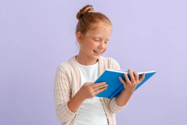 Leylak arkaplanı üzerine kitap okuyan kızıl saçlı küçük kız.
