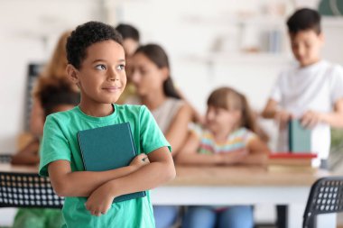 Little African-American boy with book in classroom