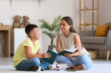 Küçük Asyalı çocuk sınıfta öğretmeniyle kitap okuyor.