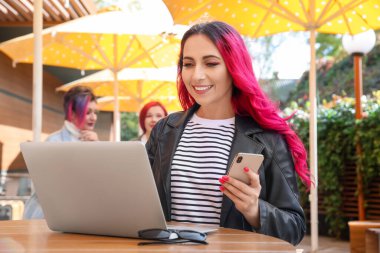 Sokağın kafesindeki masada dizüstü bilgisayarı ve cep telefonu olan güzel kadın.