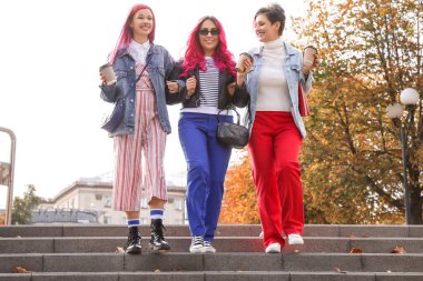 Parlak saçlı ve kahve fincanları olan güzel kadınlar aşağıda parkta yürüyorlar.