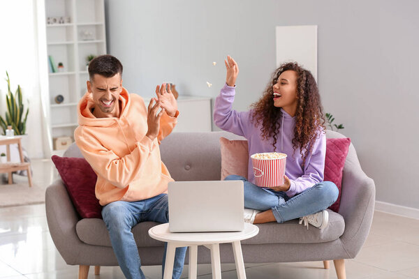 Young woman throwing popcorn at her boyfriend while watching movie at home