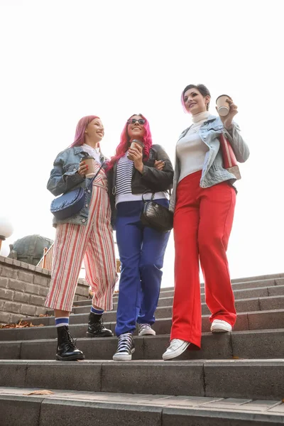 Parlak saçlı ve kahve fincanları olan güzel kadınlar aşağıda parkta yürüyorlar.