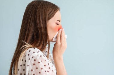 Açık mavi arka planda hapşıran genç kadın