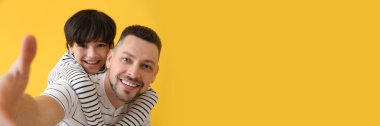 Baba ve küçük oğlu sarı arkaplanda selfie çekiyorlar.