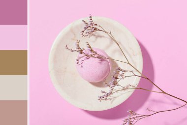 Banyo bombasıyla dolu bir kase ve pembe arka planda kuru bir dal. Farklı renk desenleri