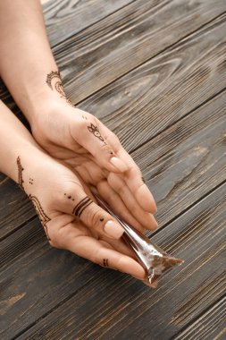Female hands with beautiful henna tattoo and paint on wooden background, closeup