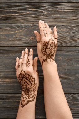 Beautiful female hands with henna tattoo on wooden background, closeup