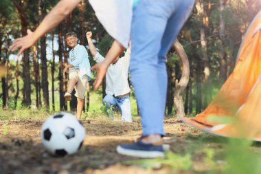 Küçük çocuk ormanda babası ve büyükbabasıyla futbol oynuyor.
