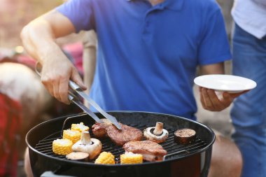 Yakışıklı adam barbekü partisinde tabağa et koyuyor, yakın plan.