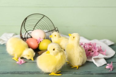 Sevimli tavuklar, ters çevrilmiş sepet. Paskalya yumurtaları ve tahta masanın üzerinde çiçekler.