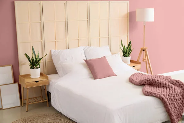 Comfortable bed, nightstands, folding screen and modern lamp near pink wall