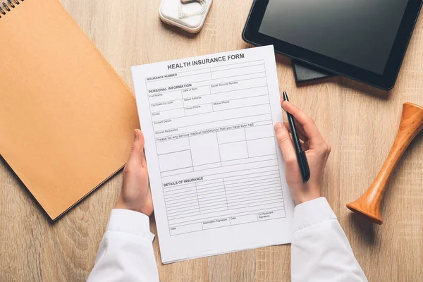 Female doctor holding health insurance form on wooden background
