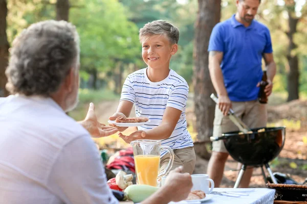 在烤肉晚会上 小男孩把烤肉盘送给爷爷 — 图库照片