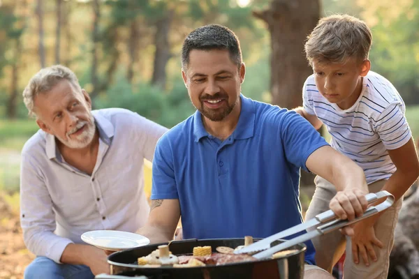 在烧烤派对上 英俊男子与他的父亲和小儿子在烤架上做饭 — 图库照片