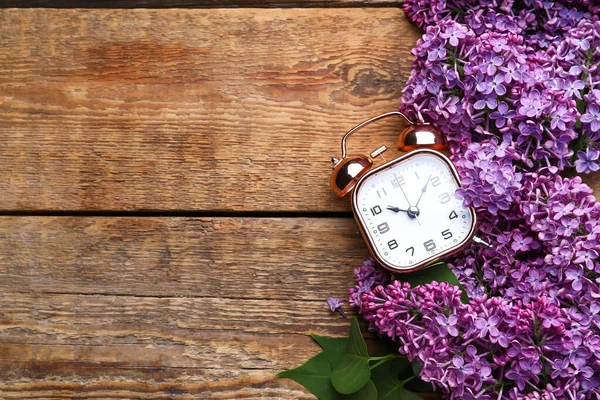 木の背景に目覚まし時計と紫のライラックの花 — ストック写真