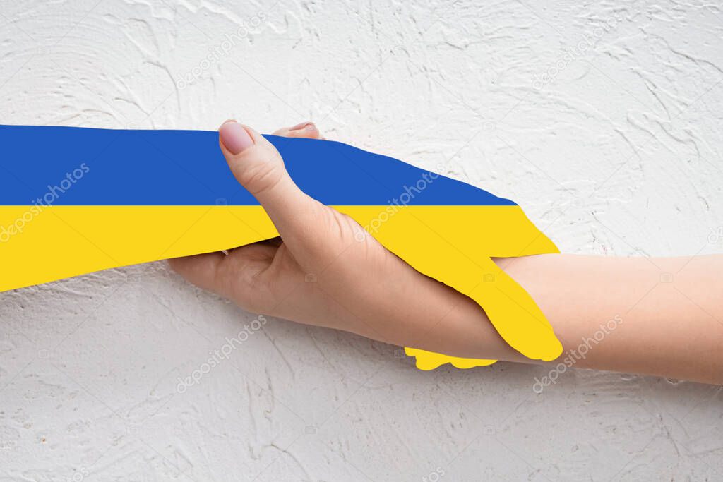 Woman holding paper hand in colors of Ukrainian flag on light background