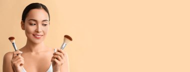 Bej arkaplanda makyaj fırçaları ve metin için yeri olan Asyalı genç bir kadının portresi