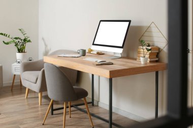 Modern computer and mobile phone on wooden standing desk near light wall