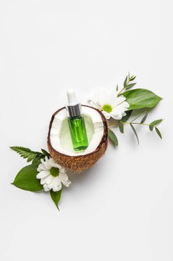 Hindistan cevizi, bitki yaprakları ve beyaz arka planda papatya çiçekli bir şişe doğal serum.
