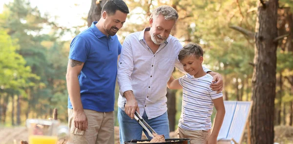 烧烤派对上 快乐的男人带着他的小儿子和父亲在烤架上做饭 — 图库照片