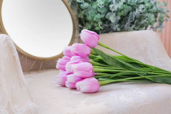 Stylish armchair with mirror and tulip flowers in room, closeup