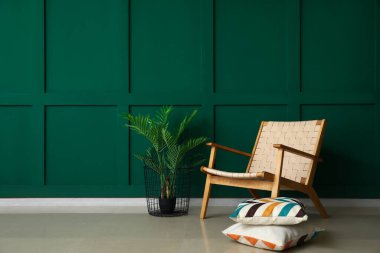 Yeşil duvarın yanında şık bir koltuk, yastıklar ve çiçek var.