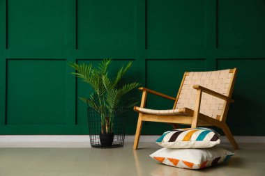 Yeşil duvarın yanında şık bir koltuk, yastıklar ve çiçek var.