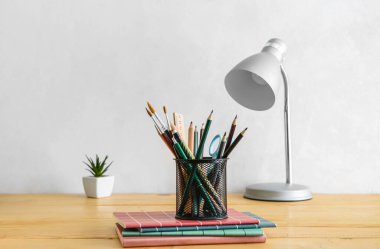 Modern lamba ve farklı kırtasiye malzemeleri ışık duvarının yanındaki masada.