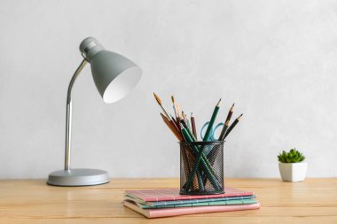 Modern lamba ve farklı kırtasiye malzemeleri ışık duvarının yanındaki masada.