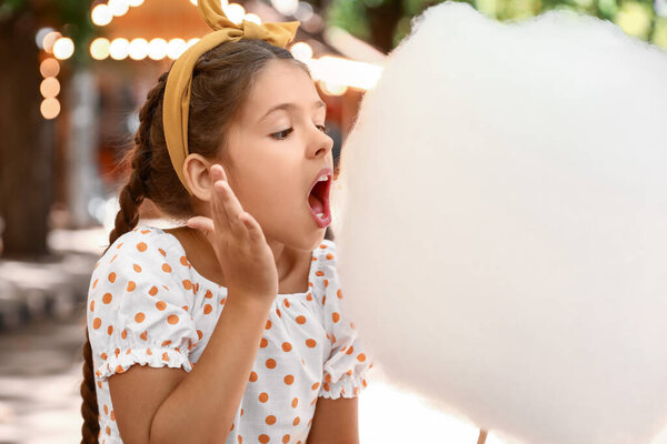 Cute little girl eating cotton candy outdoors
