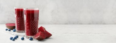 Açık arkaplanda pancar kökü ve yaban mersinli sağlıklı meyve suyu bardakları.