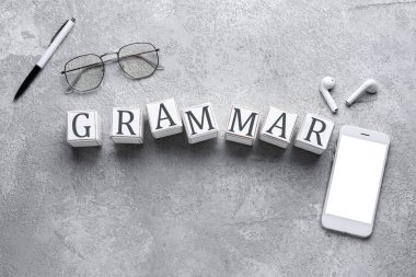Kelime GrammaR küplerden, telefondan, kalemden, kulaklıklardan ve gri arkaplanda gözlüklerden oluşur