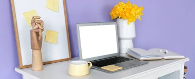 Boş ekranlı dizüstü bilgisayar, bir fincan çay, dekor ve kırtasiye malzemesi renk duvarının yanında.