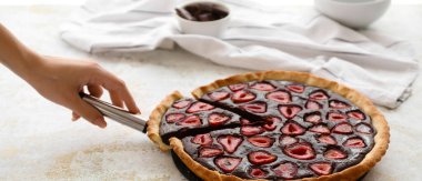 Bir kadın masadan lezzetli çikolatalı çilekli pasta alıyor.