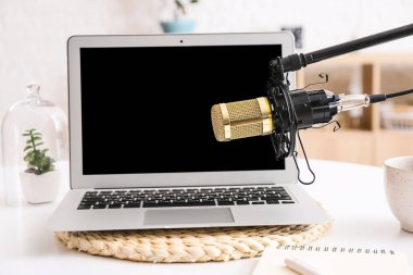 Modern dizüstü bilgisayar masada ve profesyonel mikrofonla aydınlatma odasında duruyor.