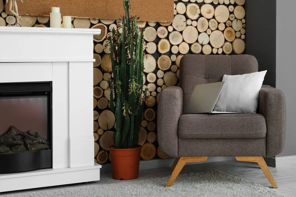 木製の壁の近くのラップトップ クッション 大きなサボテンや暖炉のあるアームチェア — ストック写真