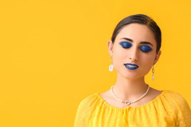 Sarı arka planda olağandışı makyajı olan çekici genç bir kadın.