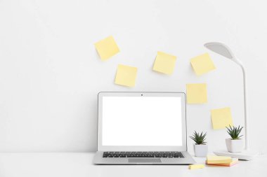 Boş yapışkan notlar, modern laptop, ev bitkileri ve lamba beyaz duvarın yanındaki masada.