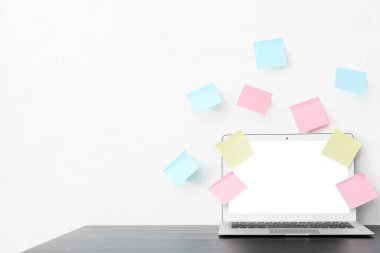 Koyu masada modern laptop ve beyaz duvarda farklı yapışkan notlar.