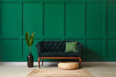 Yeşil duvarın yanında palmiye yaprakları olan şık bir kanepe ve vazo.